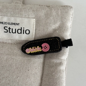 Detail of black denim bow hair clip with Wink patch and pink button on canvas