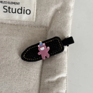 Macro detail of black denim hair clip with a cute pink bear charm and blue party hat
