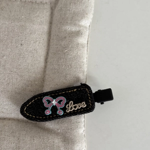 Detail of denim bow hair clip with yellow stitching and decorative Love letter lettering