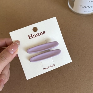 Detail view of two lavender matte oval hair clips displayed on a brand card