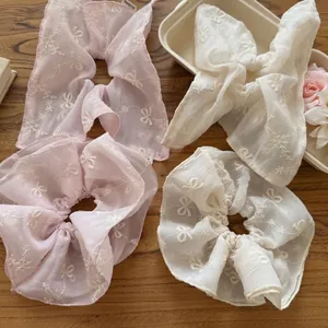 Pink and beige mesh scrunchies and bow hair clips with floral embroidery on a wood table