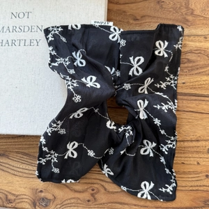 Elegant black satin hair scrunchie with white bow patterns and branded woven label