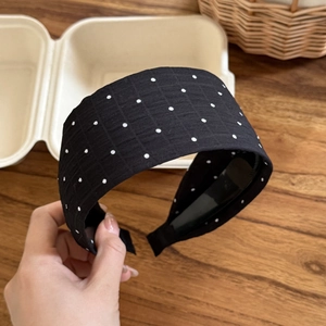 Polka dot wide headband in black and white fabric displayed on a rustic wood background