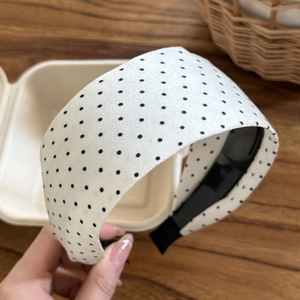Close-up of a wide fabric headband with classic black polka dots on white background