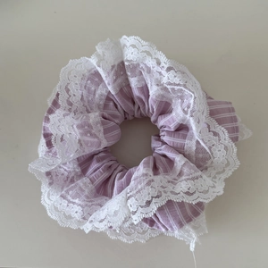 Detailansicht eines lila gestreiften Stoff-Scrunchies mit eleganter weißer Spitzenstickerei