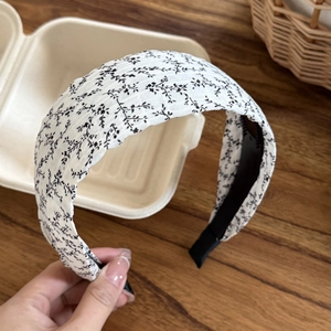 Detail of floral white wide headband with black leaf patterns on a rustic wooden background
