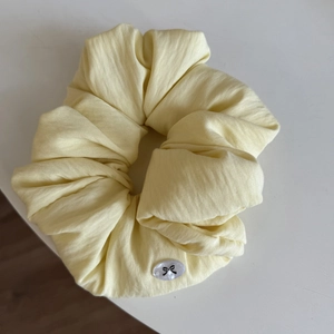 Creamy yellow scrunchie with textured fabric and small bow charm on white background