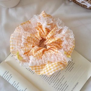 Sweet yellow plaid scrunchie with lace trim and bow, placed on an open book