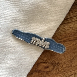 Détail de la barrette en denim avec lettrage en strass et bordure en métal argenté