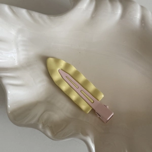 Dettaglio della clip per capelli ondulata gialla e rosa su un piatto a forma di conchiglia