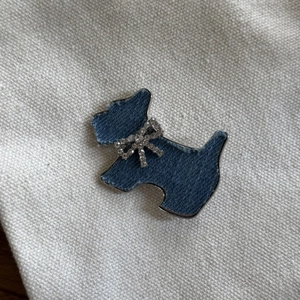 Détail d'une broche chiot en denim avec bords argentés et un nœud en strass étincelant