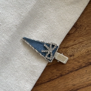 Détail d'une pince à cheveux en denim bleu avec nœud en strass et bordure ondulée