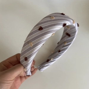 Detailed texture of striped lace fabric hair tie with decorative fuzzy pom-poms