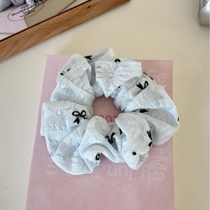Detailansicht eines hellblauen Spitzen-Scrunchies mit eleganten schwarzen Bogen-Stickereien