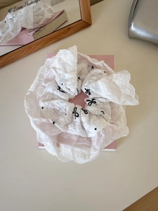 Nahaufnahme von weißem Spitzen-Haargummi mit schwarzen Schleifen-Stickereien auf Buch