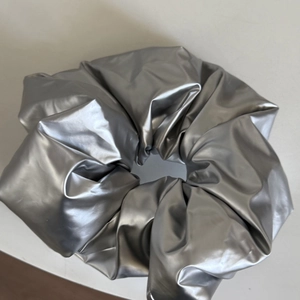 Detail eines silbernen Metallic-Scrunchies mit glänzend beschichtetem Stoff und Falten