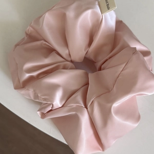 Nahaufnahme eines rosa Satin-Haargummis mit handgefertigtem Etikett und weicher Textur