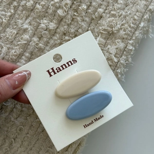 Dettaglio di fermagli per capelli ovali crema e blu presentati su una carta bianca