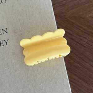 Dettaglio di una molletta per capelli giallo crema a forma di onda su un libro e legno