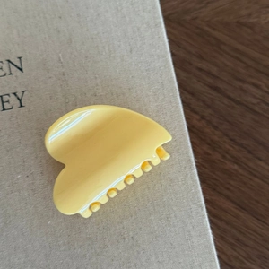 Primo piano di una molletta per capelli giallo crema minimalista con finitura lucida su un libro
