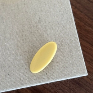 Dettaglio della clip per capelli ovale minimalista in resina giallo crema su lino