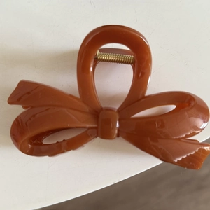 Detailed view of a brown bow hair claw clip with glossy finish and metal spring