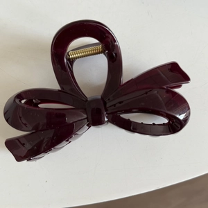 Detailed view of the dark burgundy bow-shaped hair claw clip with golden metal spring