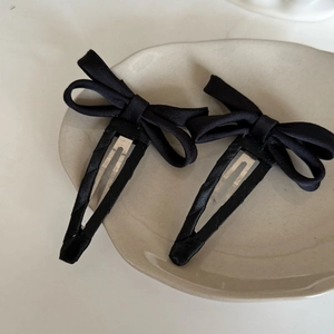 Set of two black satin bow hair clips on a minimalist beige ceramic plate