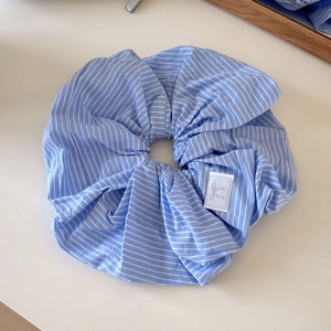 Blue and white striped scrunchie with bow logo tag displayed on beige surface