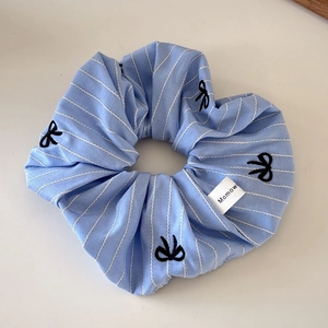 Detail of light blue striped scrunchie featuring black embroidered bows and brand tag