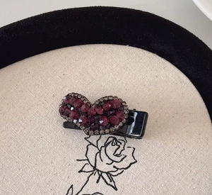 Gros plan détaillé d'une pince à cheveux en forme de cœur avec strass bordeaux sur tissu