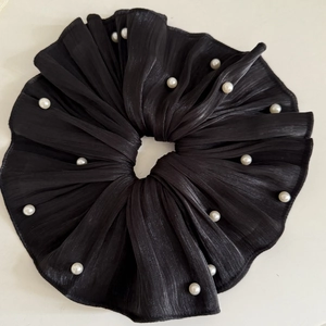 Gros plan sur chouchou en tissu plissé noir avec accents de perles blanches et texture