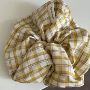Detail of yellow plaid scrunchie featuring a white hand made fabric label on white background