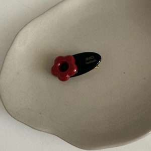 Close-up of handmade oval hair clip with 3D red flower on beige ceramic tray