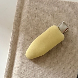 Minimalist creamy yellow fabric drop hair clip on neutral textured linen book cover background