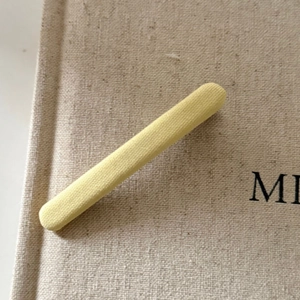 Detail of a light yellow fabric hair clip showing soft knit texture on beige background