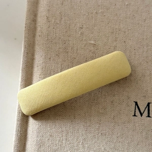 Detail of light yellow fabric snap hair clip with knit texture on a rustic book cover