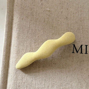 Close-up of a wavy cream-yellow fabric-covered BB hair clip on a textured background