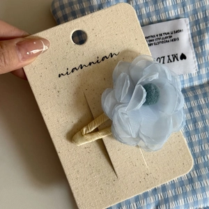 Detail of light blue fabric flower hair clip on display card with blue plaid background