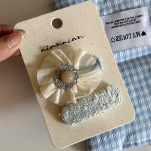 Detail of blue tweed rectangular clip and cream fabric flower hairclip on a card