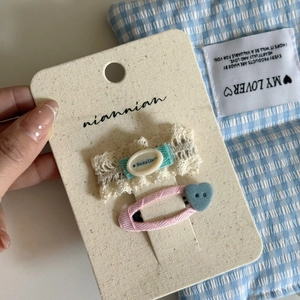 Close-up of blue lace and pink twill hair clips with heart button on display card