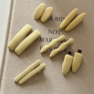 Set of 6 creamy yellow fabric hair clips in various shapes on a minimalist background