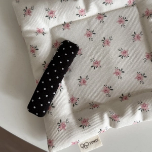 Close-up of elegant black fabric hair clip with white polka dots on soft floral cushion