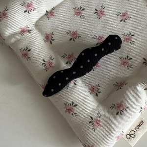 Detail of French style black hair clip with white polka dots on soft floral fabric