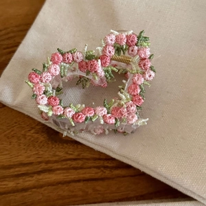 Close-up of pink and green floral embroidery on a heart-shaped transparent hair claw clip
