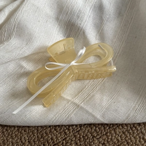 Detail of light yellow acrylic hair claw clip with elegant white silk ribbon bow tie