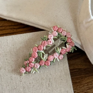 Close-up of pink sunset floral embroidery and green leaves on a sweet BB hair clip