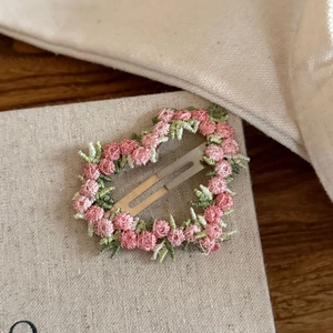 Macro detail of heart-shaped embroidered hair clip with pink flowers and green leaves