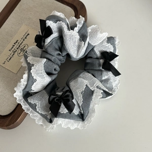Close-up of grey fabric scrunchie with white lace trim and black silk bow accents