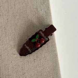 Detail of red plaid hair clip with cherry charms and wavy fabric edges on a beige textile